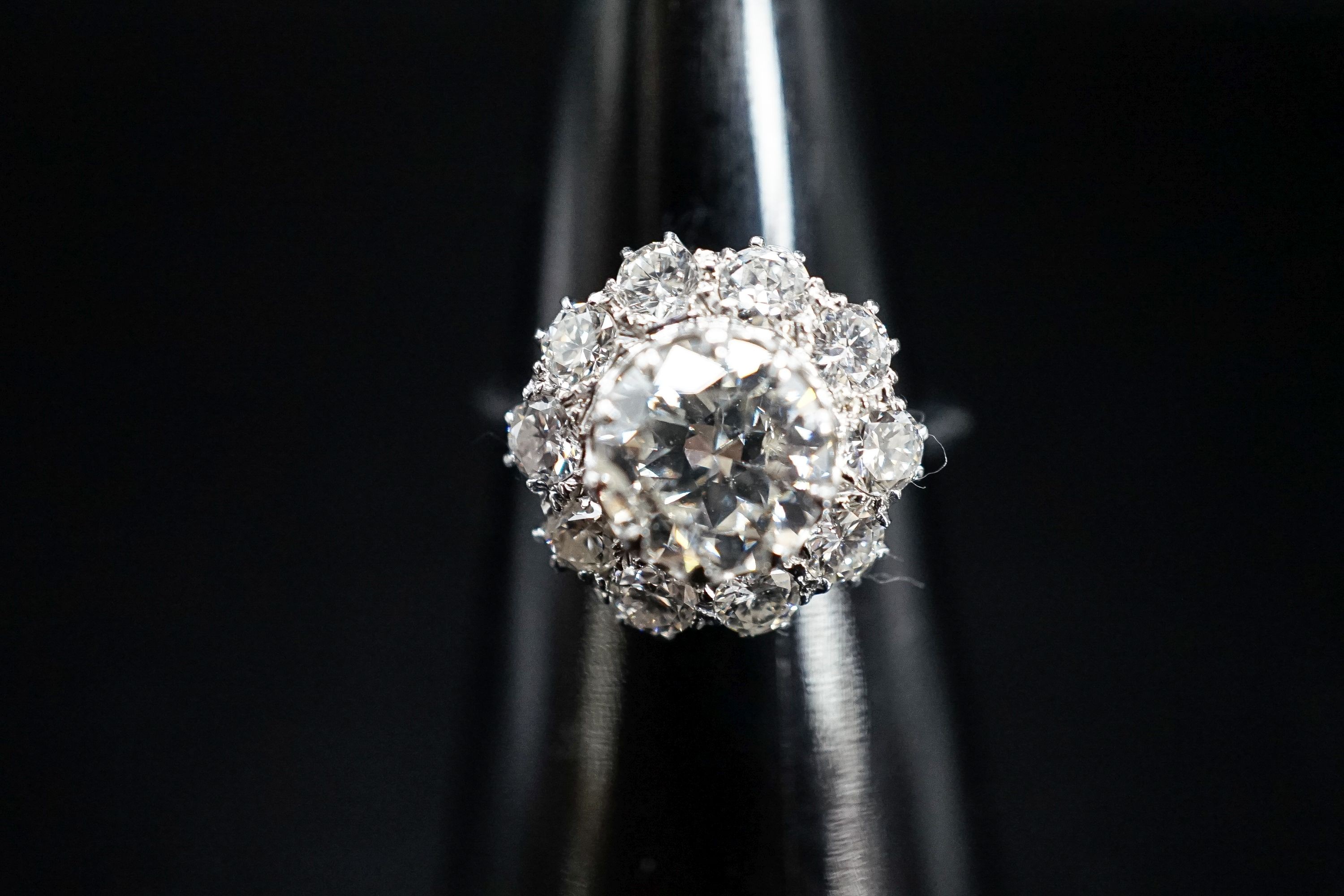 A white metal and eleven stone diamond set flower head cluster ring, the central stone weighing approximately 1.60ct, size N, gross 5 grams